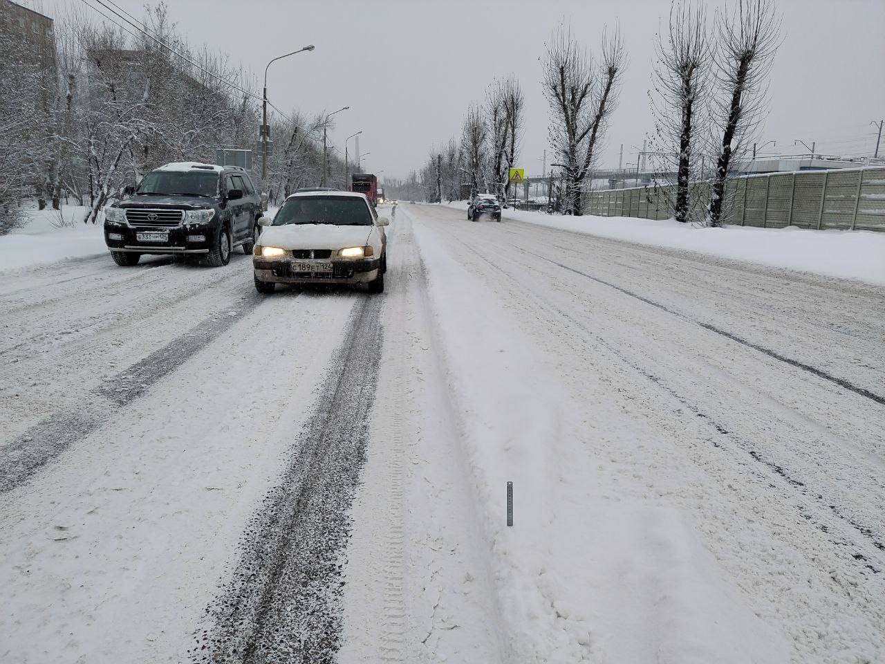 машины едут по заснеженной дороге в красноярске